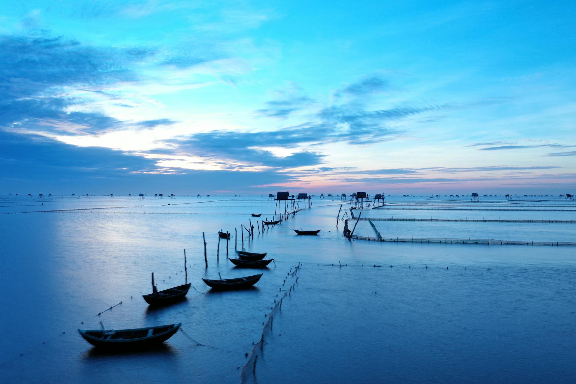 Serene sunrise over moored fishing boats at Thai Binh, Vietnam. Calm waters under a vibrant sky.