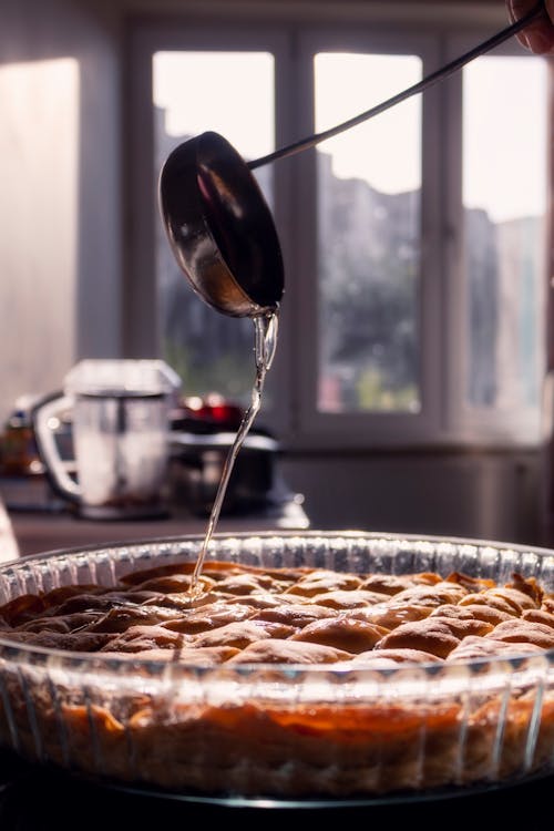 A person pouring syrup on a pie in a kitchen
