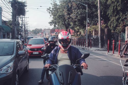 Free Motorcyclists navigate busy urban streets surrounded by city traffic and trees. Stock Photo