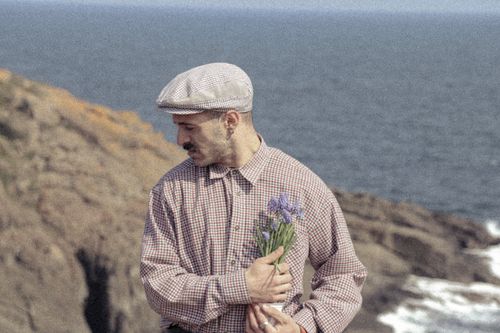 Free Man in vintage attire holding flowers by Istanbul coastline. Stock Photo