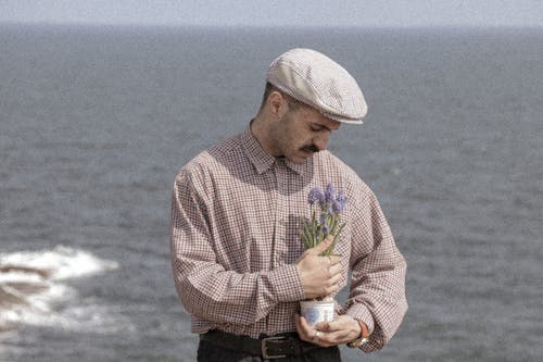Man in Beret Posing with Flowers on Seashore