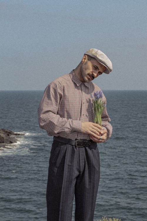 Free Elegant man with a bouquet, standing against a scenic ocean backdrop, showcasing fashion and nature. Stock Photo