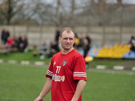 Male football player in red jersey on outdoor field during daytime match.