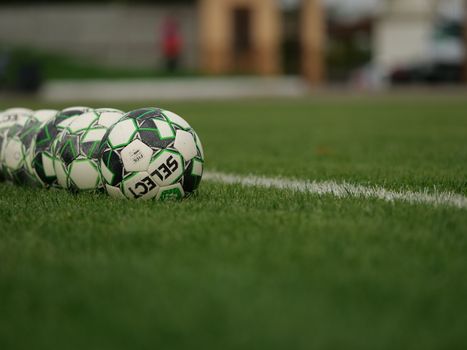 Close-up view of soccer balls lined up on a grassy football field.