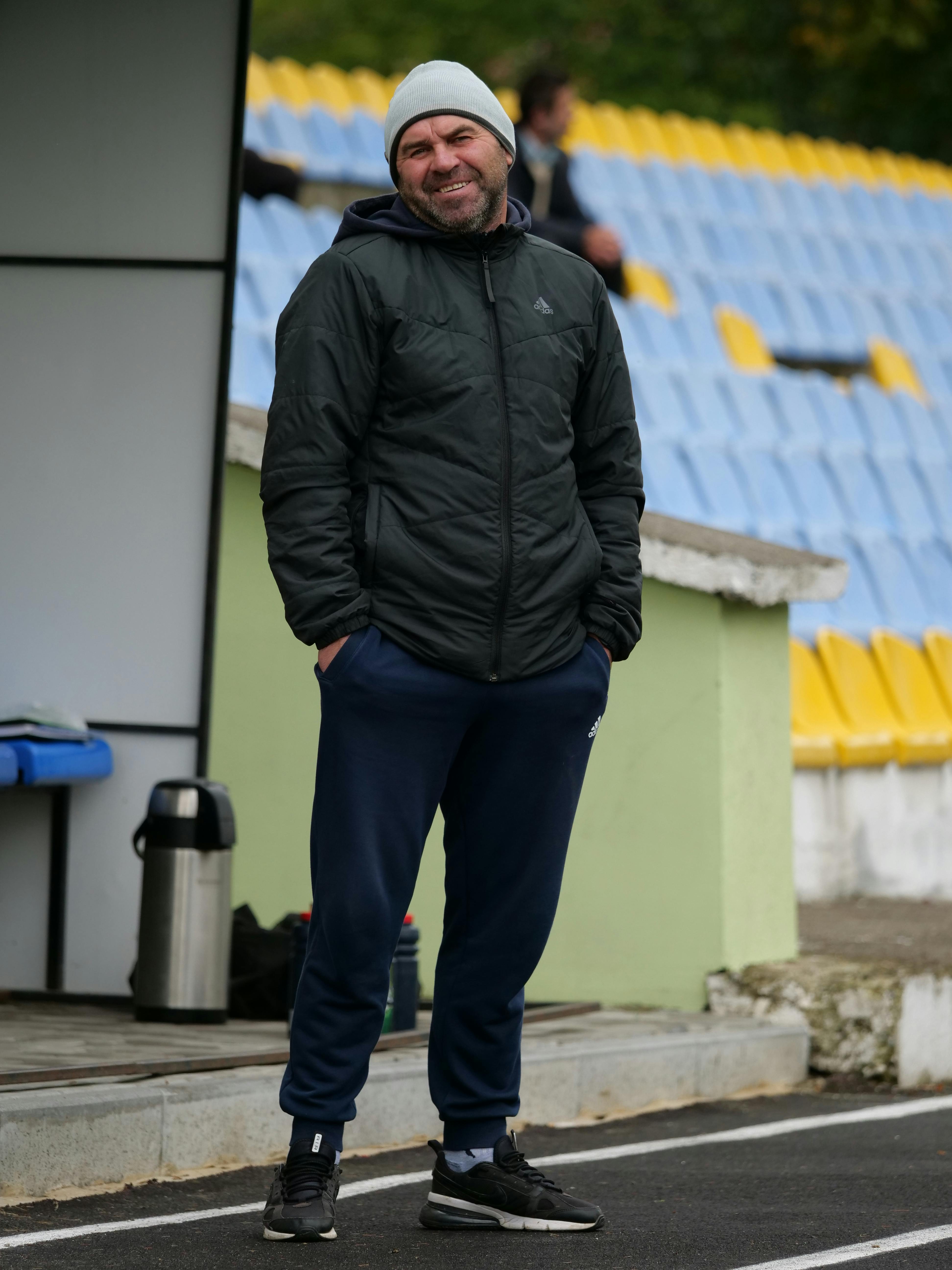 A sports coach in casual winter attire stands by empty stadium seats. Perfect for sports-related themes.