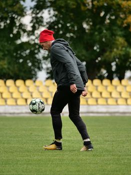 Man practicing soccer dribbling on a football field, wearing a red hat and black attire.