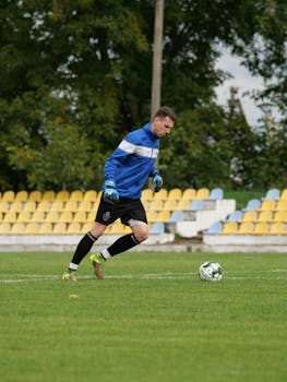 Goalkeeper training on outdoor soccer field with green grass and empty stands.