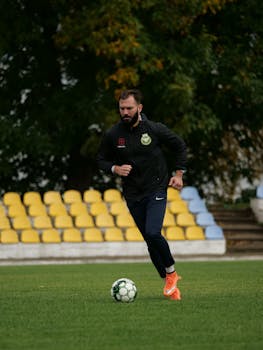 A soccer player in sportswear practices on a grassy field with empty stadium seats.