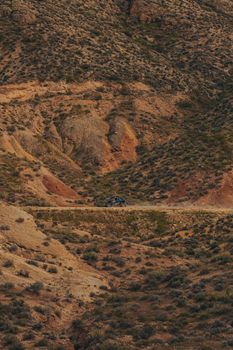 A blue 4x4 driving through arid mountain terrain on a dirt road, captured in a drone shot.
