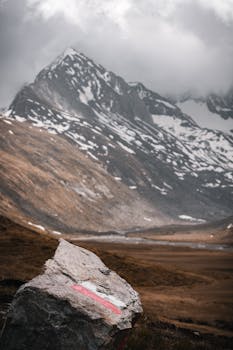 Scenic view of snowy mountain peaks in Obergurgl, Austria with a marked hiking trail rock in the foreground.