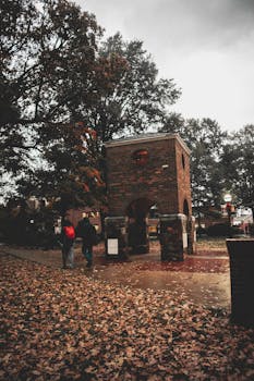 A couple walking by a historic brick structure in a park filled with autumn leaves.