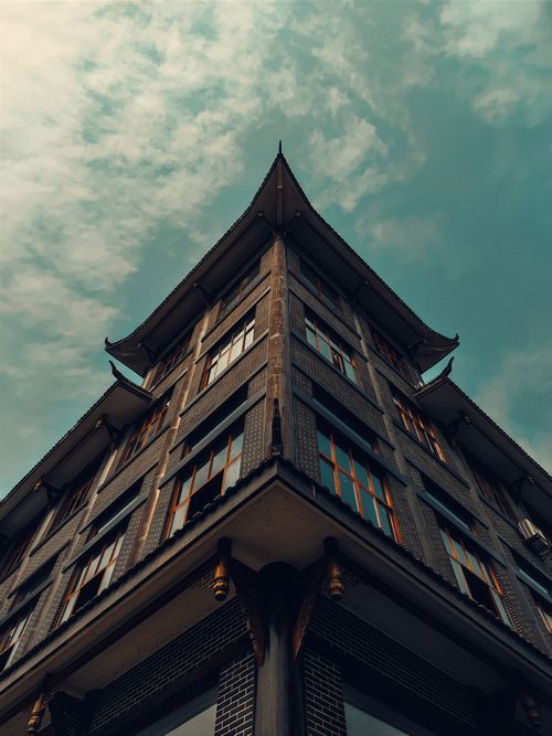 Free A striking low angle view of a modern building with pagoda-style architecture against a cloudy sky. Stock Photo