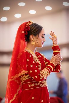 An Indian bride wearing a red saree with intricate embroidery, adorned in traditional jewelry.