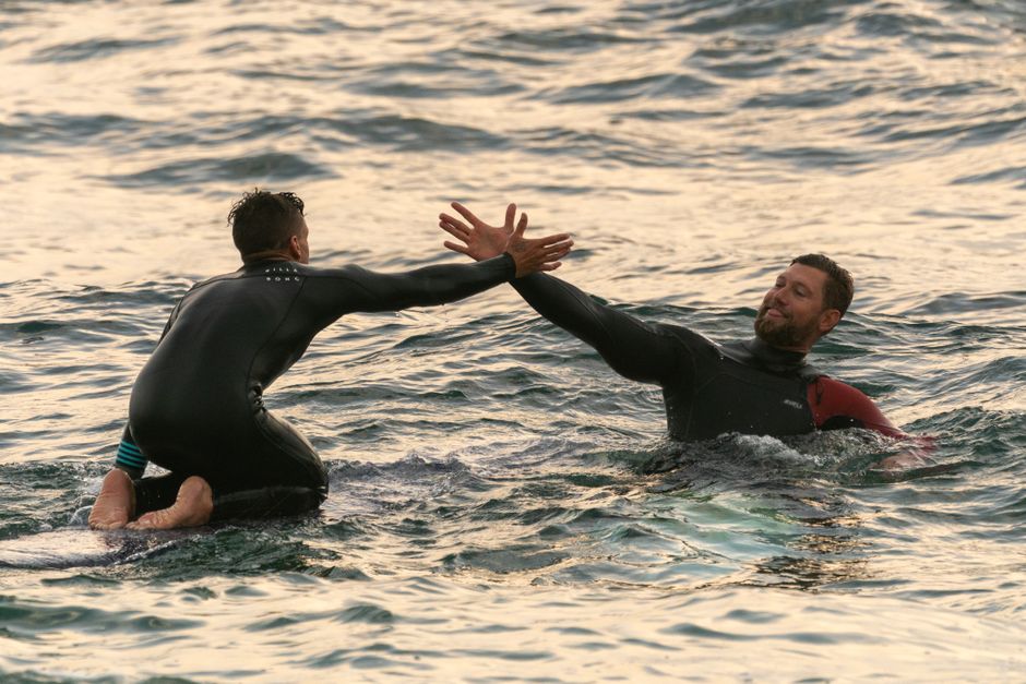 Two male surfers high-five in the ocean, enjoying water sports and teamwork.