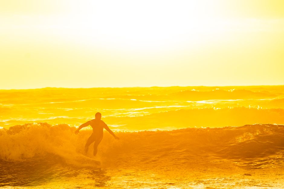 A silhouette of a surfer catching waves in the vibrant golden hour light at the ocean shoreline.
