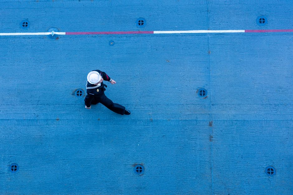 A top-down shot capturing a navy sailor walking on a ship's blue deck.