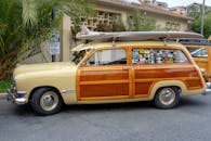 一辆经典的伍迪旅行车停在户外，车顶上放着一块老式冲浪板