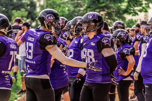 American football team in purple jerseys discussing strategy outdoors.