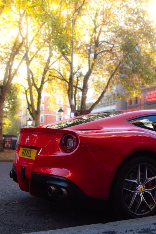 Free Back view of a red Ferrari F12 Berlinetta on a vibrant city street in London during fall. Stock Photo