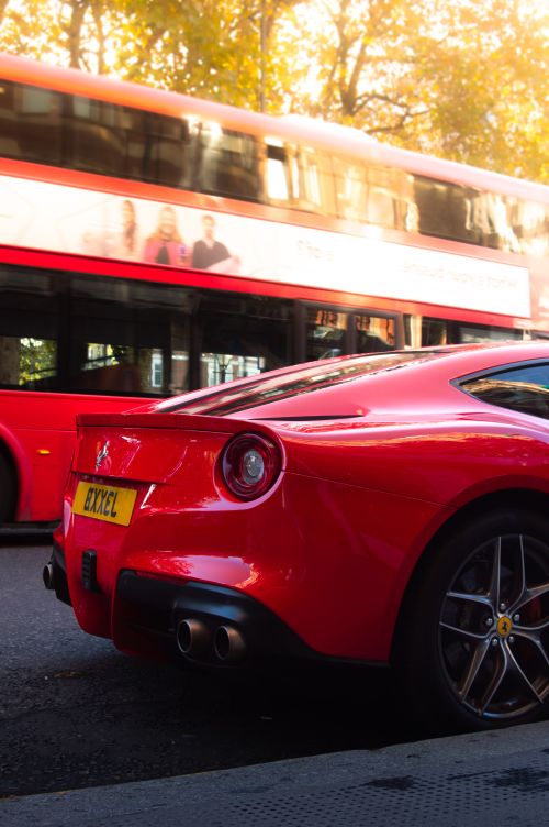 Free A sleek red supercar parked in London with a blurred double-decker bus passing by. Stock Photo