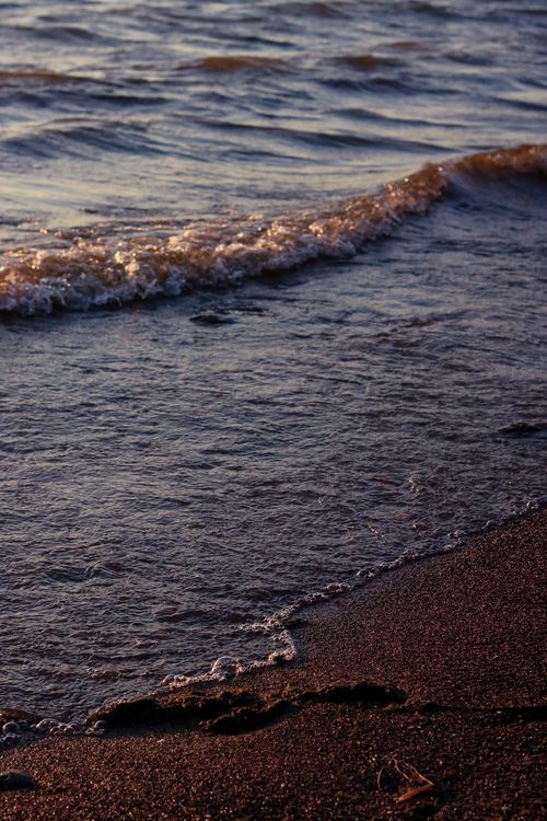 Free Serene view of gentle waves lapping against the sandy shore at sunset, capturing nature's calmness. Stock Photo