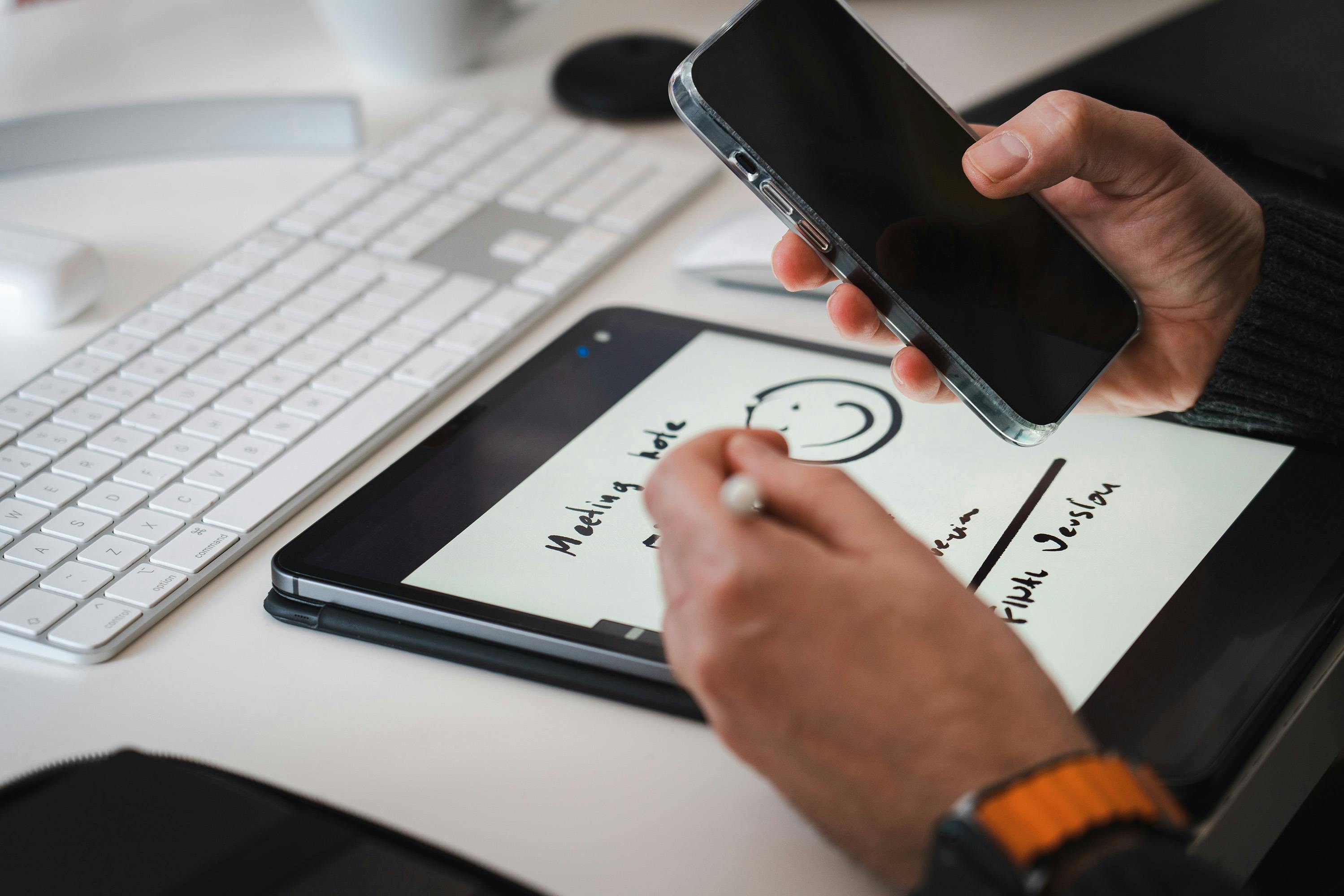 Hands using a stylus on a tablet for note-taking alongside a smartphone, suitable for tech themes.