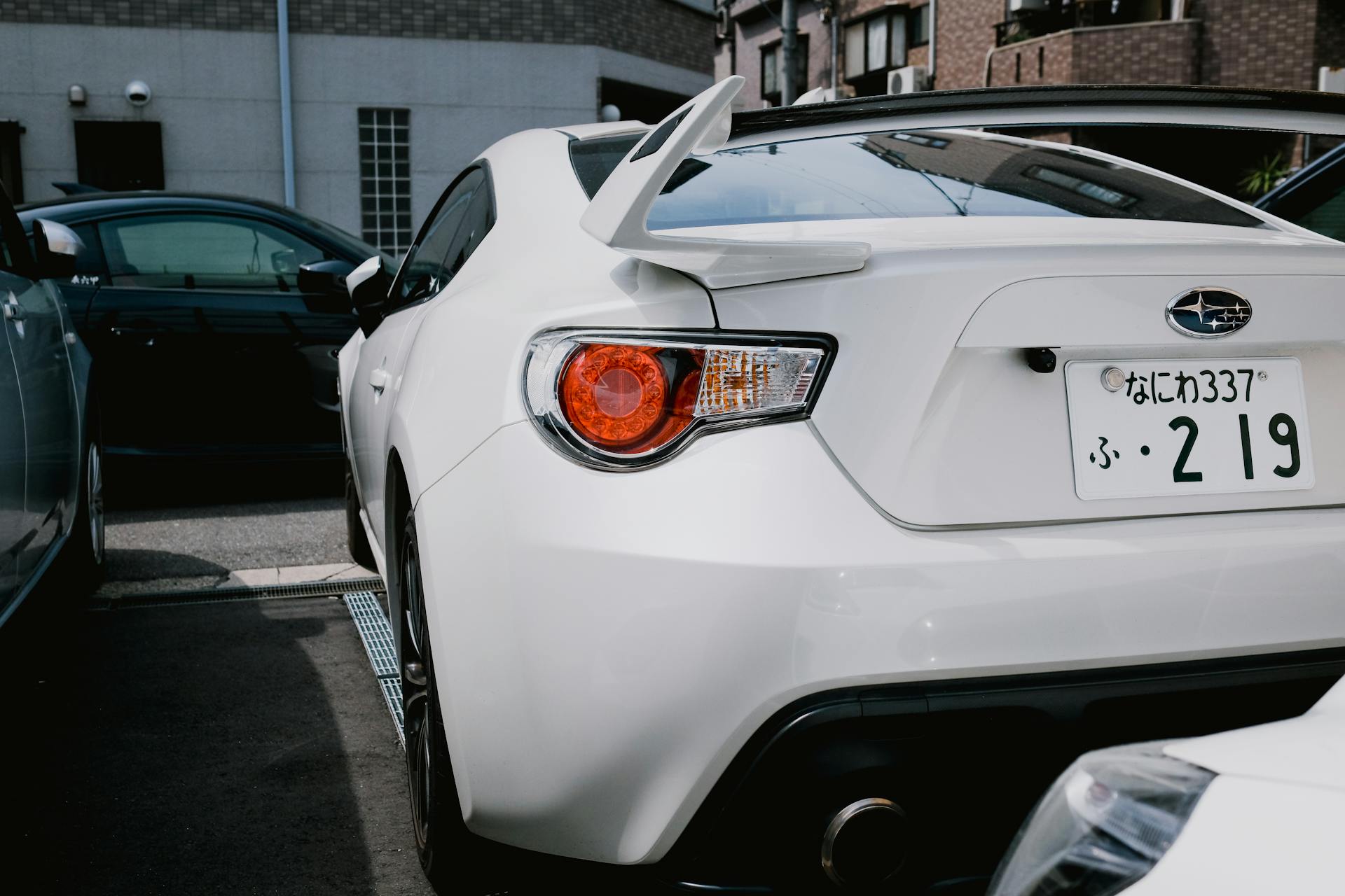 A stylish white Subaru BRZ parked in a city lot, showcasing its sporty rear design.