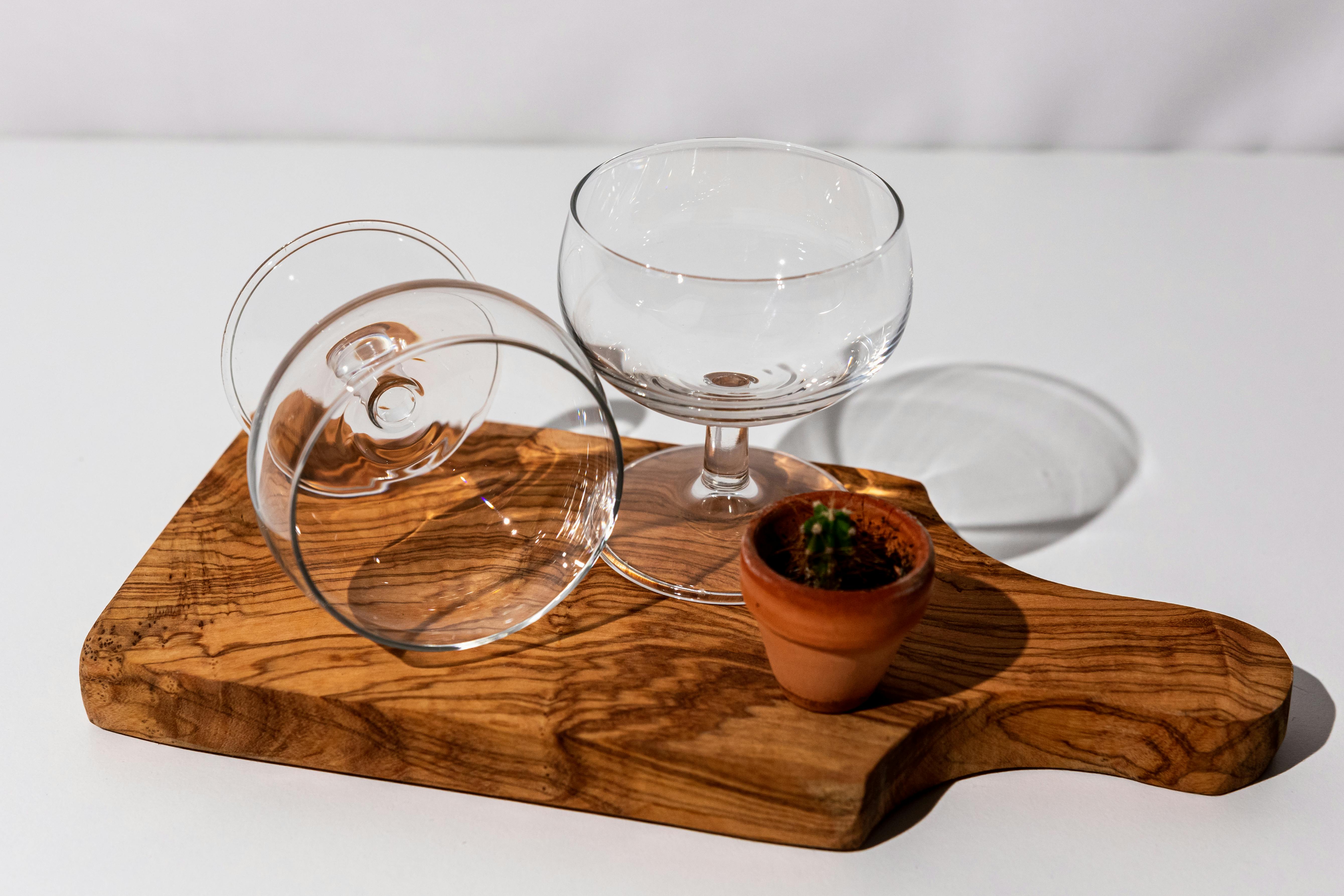 a wooden cutting board with two glasses and a plant