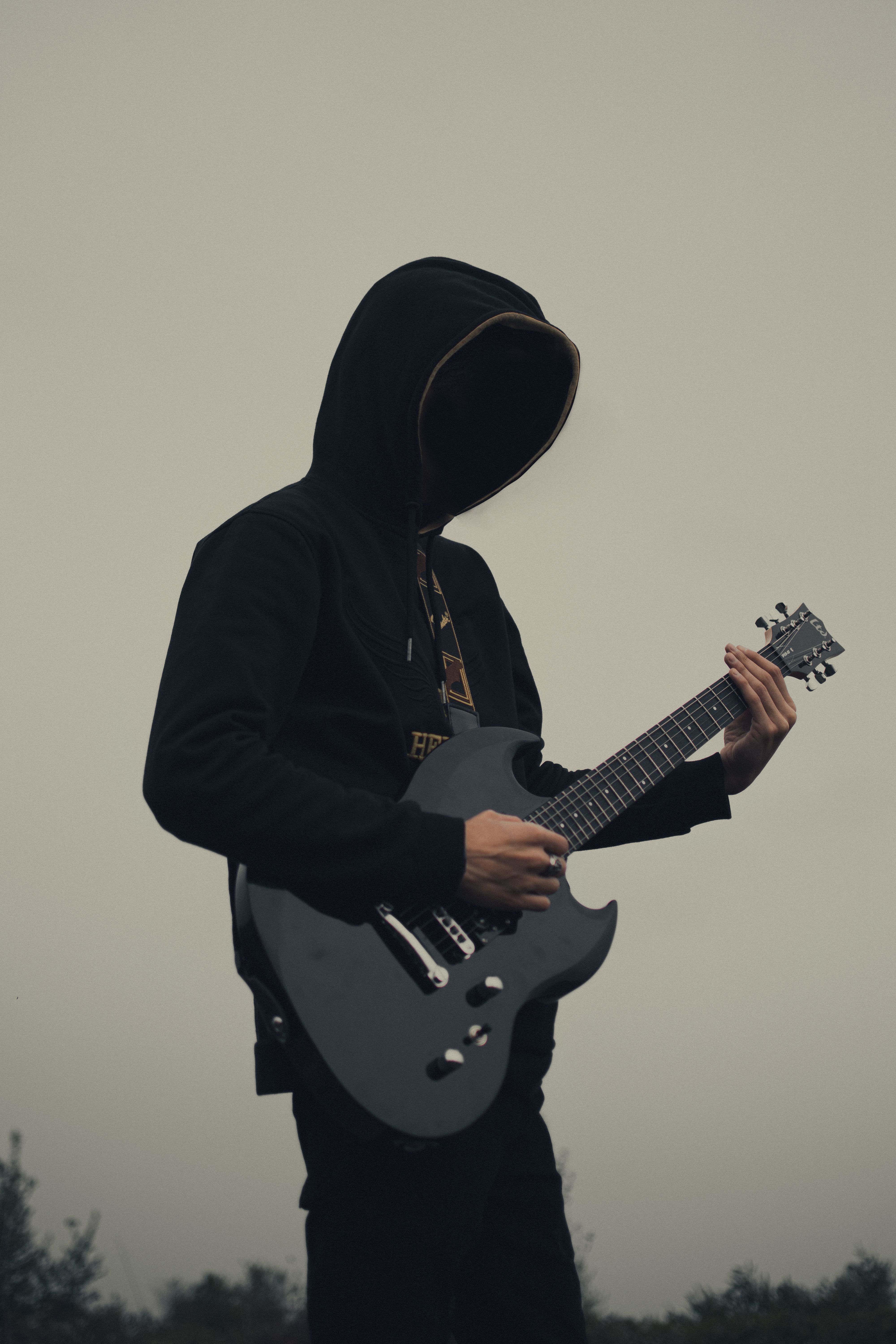 Silhouette of a hooded musician playing an electric guitar outdoors.