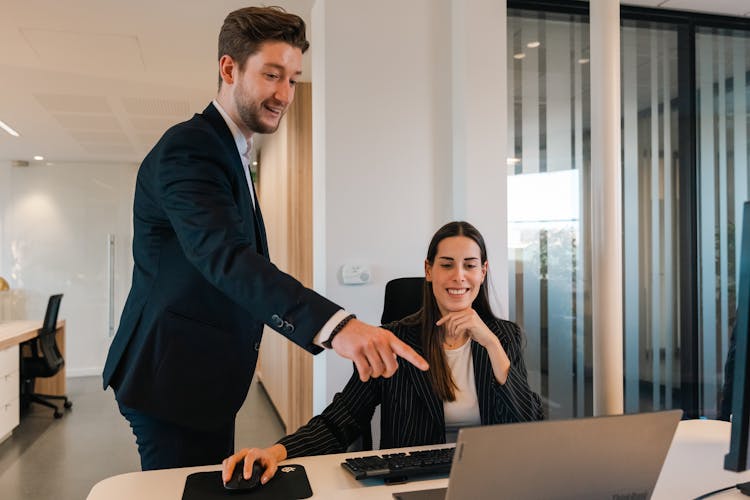 Woman Sitting At The Desk In An Office And Man Pointing At Her Computer 