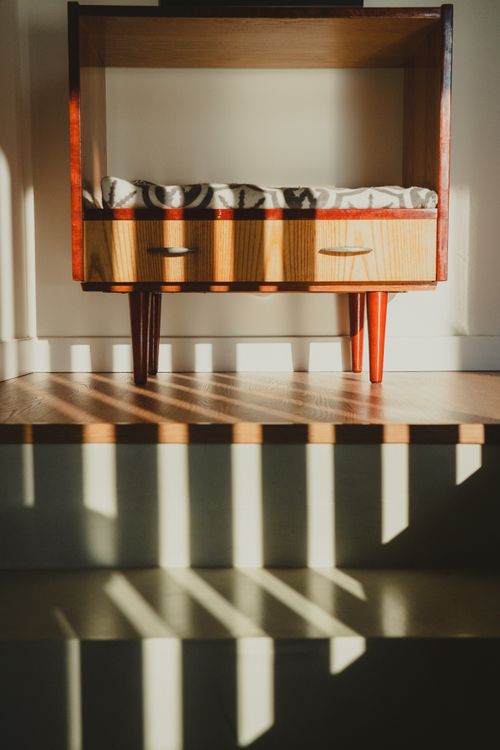 Free A modern wooden cabinet with shadows creating artistic patterns on the floor. Stock Photo