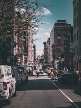 A bustling urban street with construction workers, cars, and tall buildings under a bright sky.