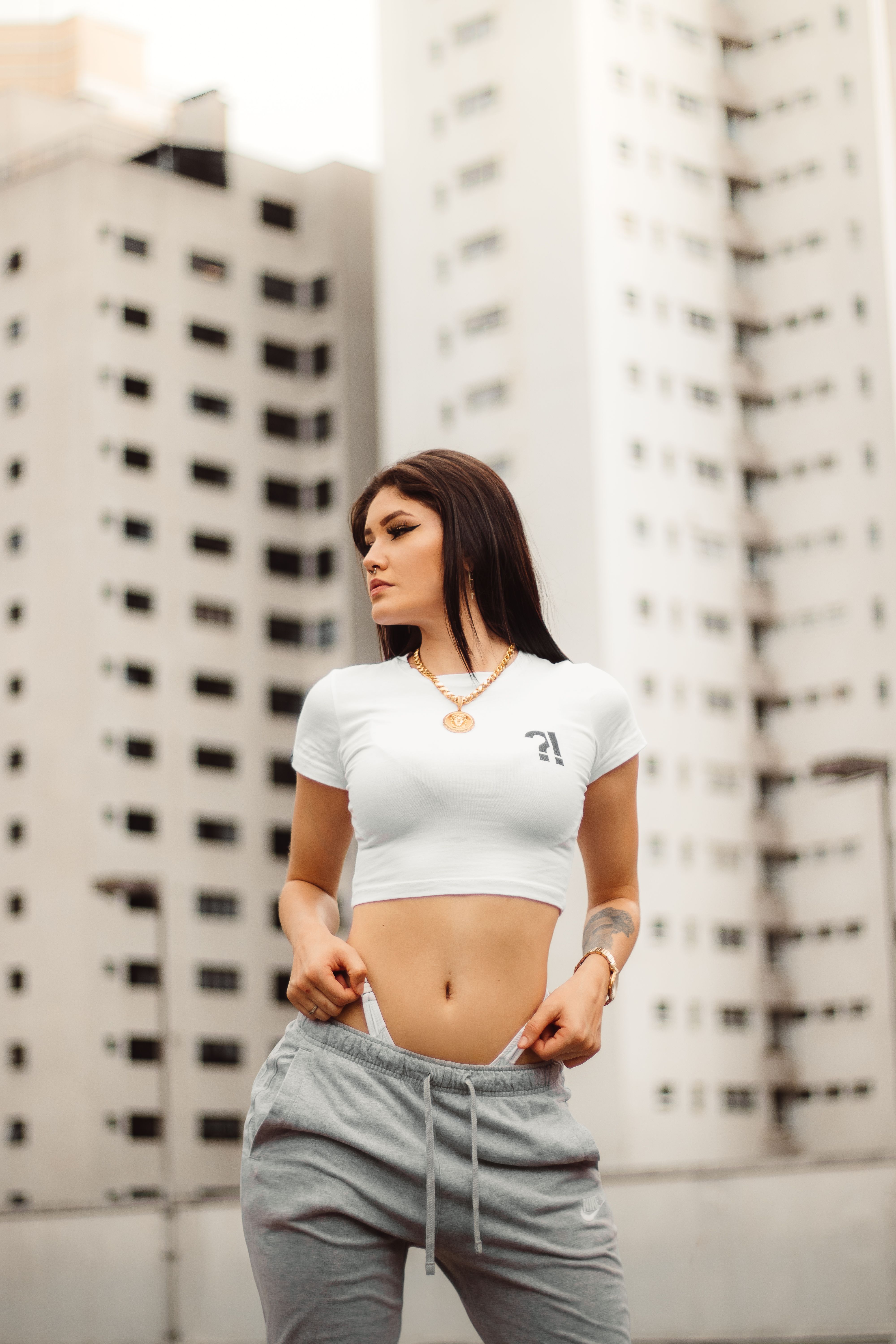Young woman in trendy fashion poses against high-rise buildings, capturing urban style.