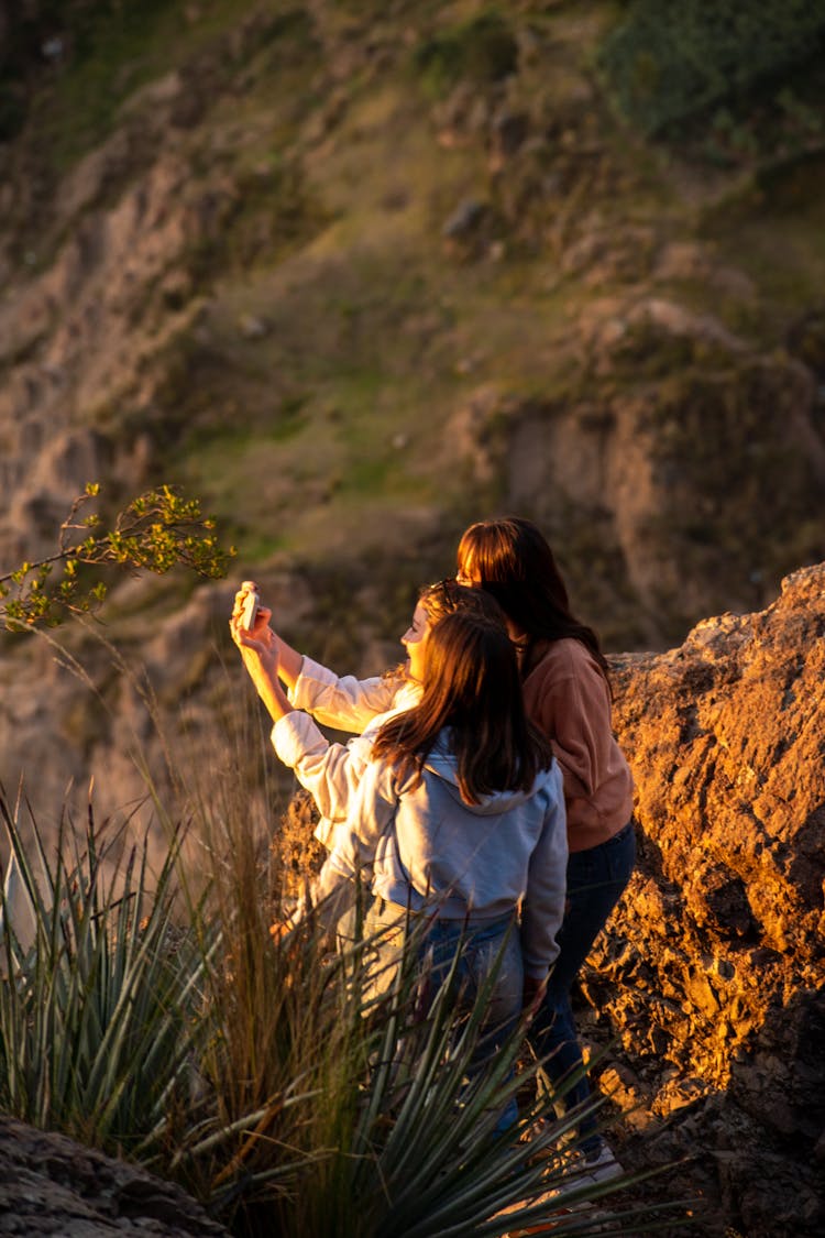 Smiling Girls Taking Pictures On Rock On Sunset