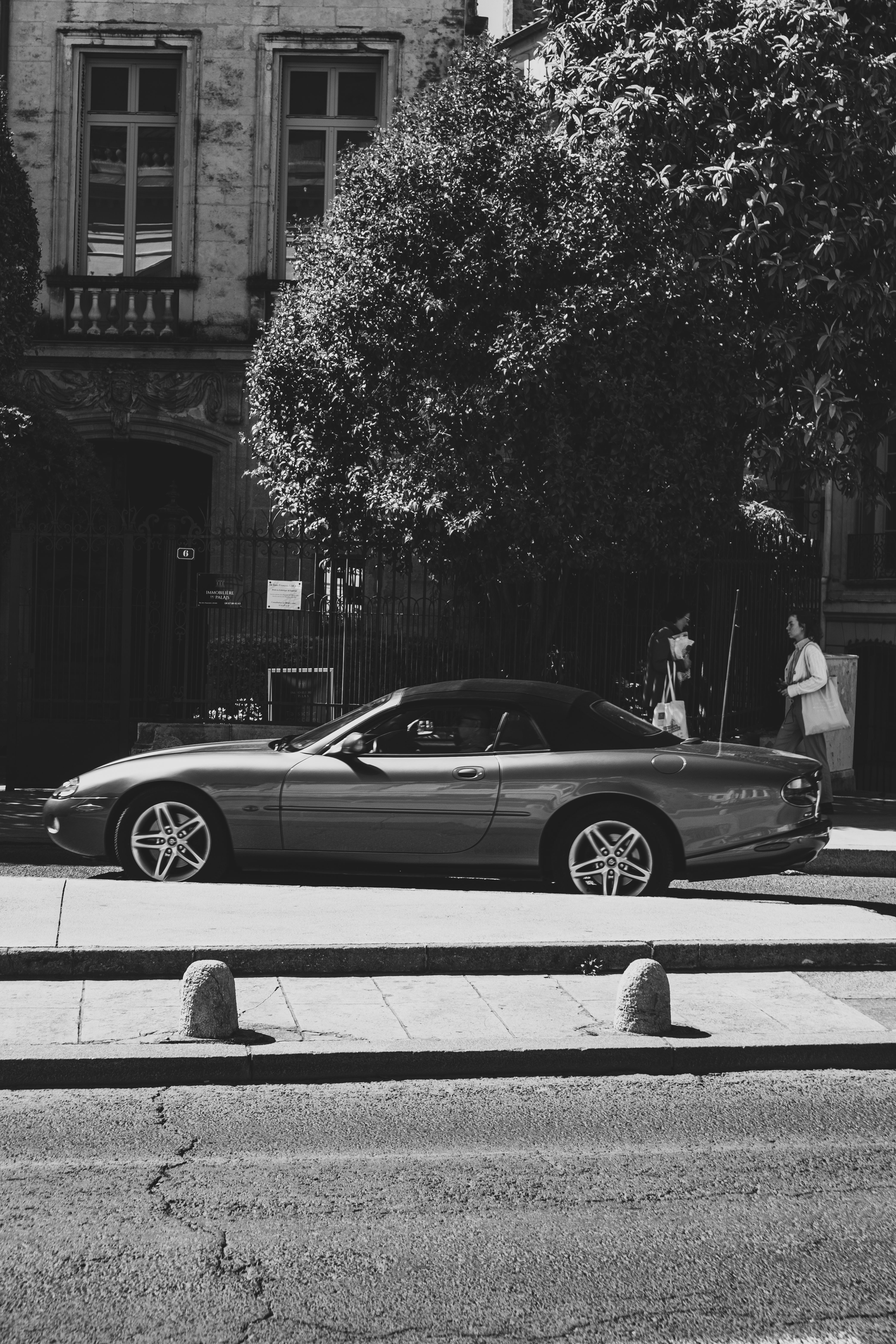 Fotomural Imagen en blanco y negro de un convertible de lujo aparcado en una calle de la ciudad iluminada por el sol.