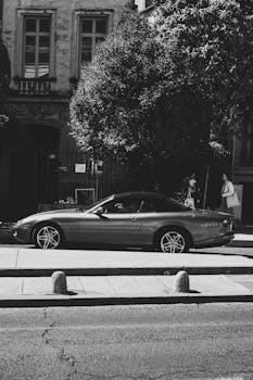 Black and white image of a luxury convertible parked on a sunlit city street.