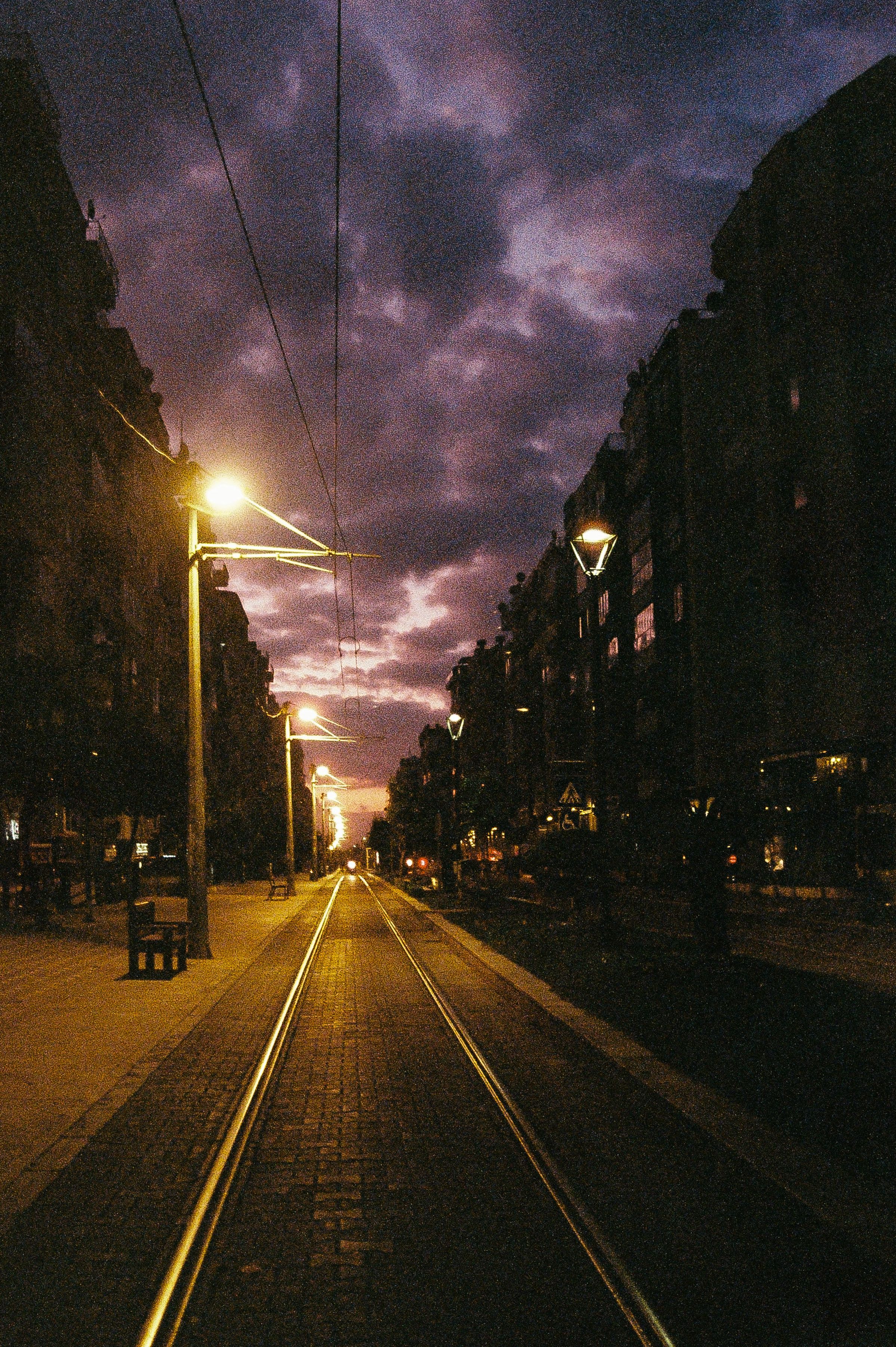 Atmospheric city street scene with tram tracks at dusk under stormy skies.