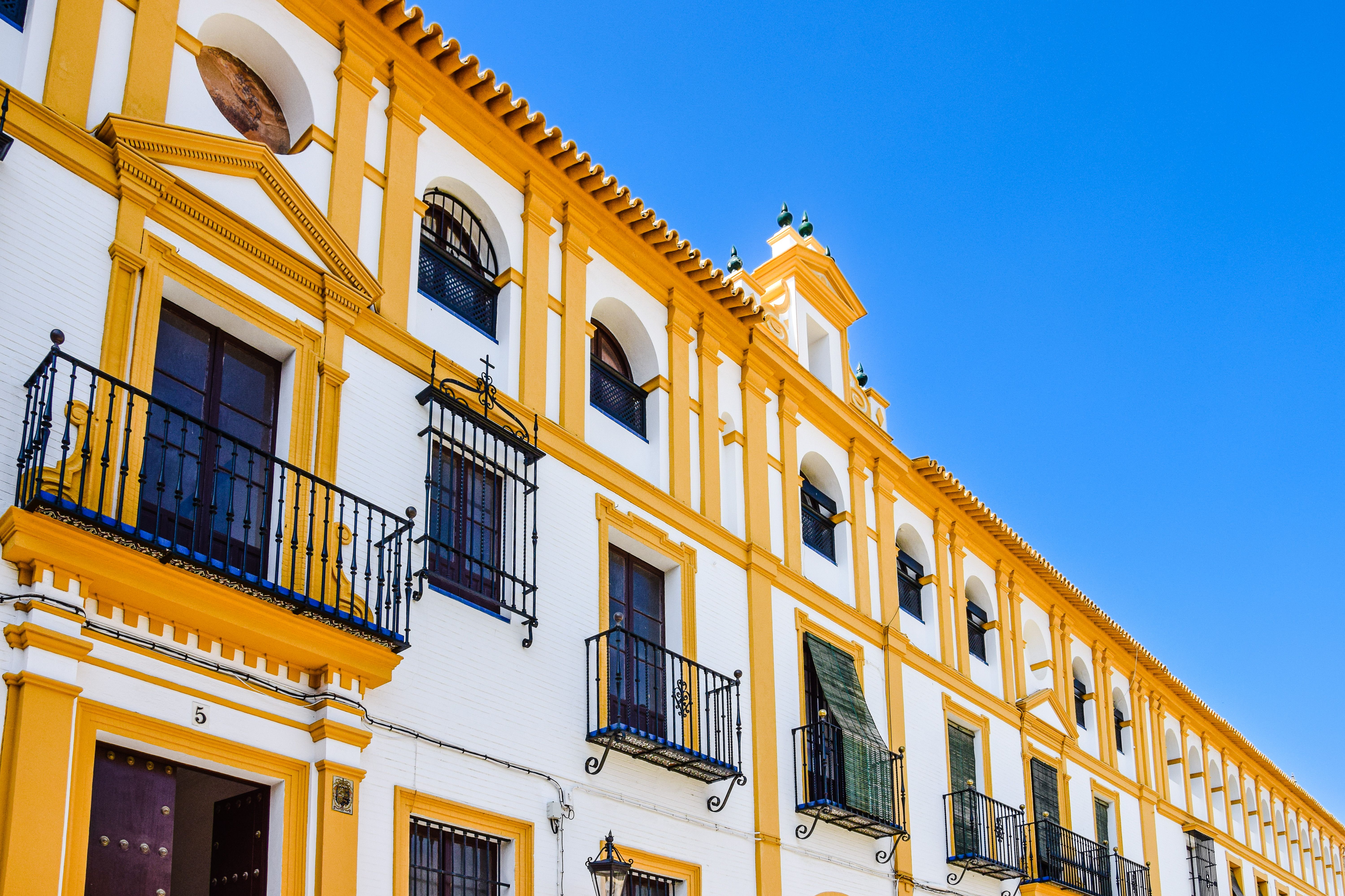 Elegant yellow and white facade of a historic building with balconies in Seville, Spain.