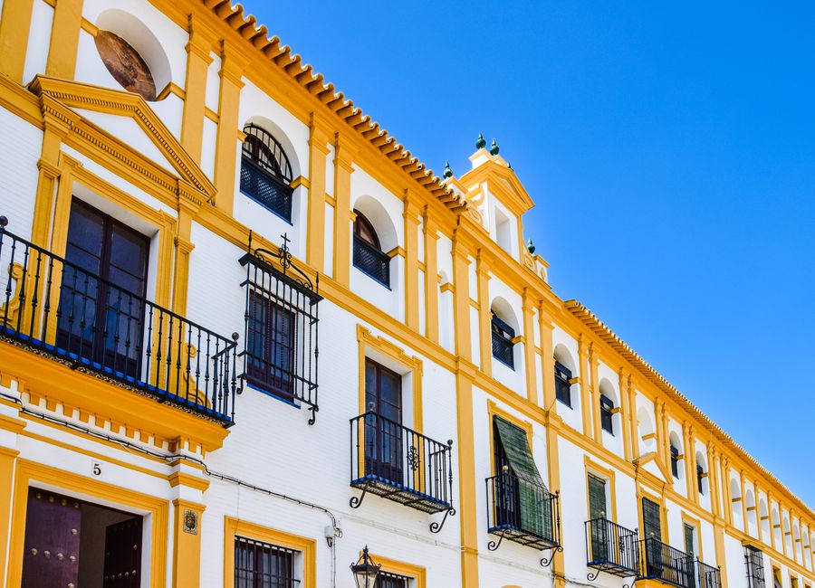 Elegant yellow and white facade of a historic building with balconies in Seville, Spain.