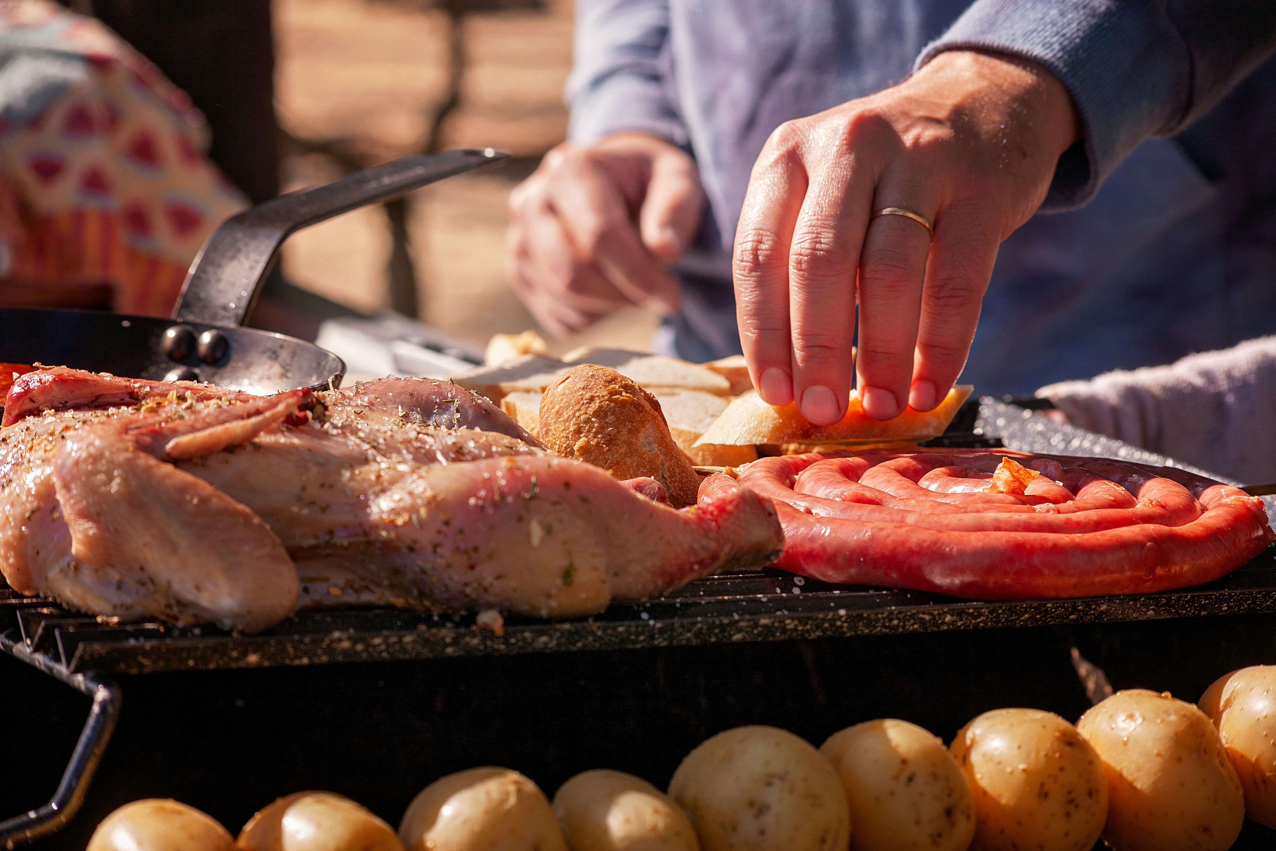 A close-up of a lively outdoor barbecue featuring chicken, sausages, and bread on a grill.