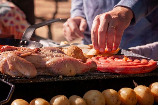 A close-up of a lively outdoor barbecue featuring chicken, sausages, and bread on a grill.