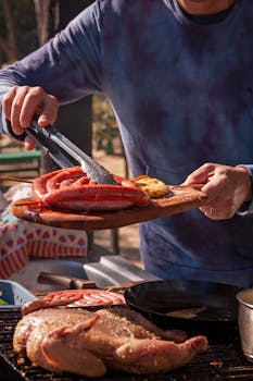 Man grilling assorted sausages and meat outdoors, serving on a wooden platter.