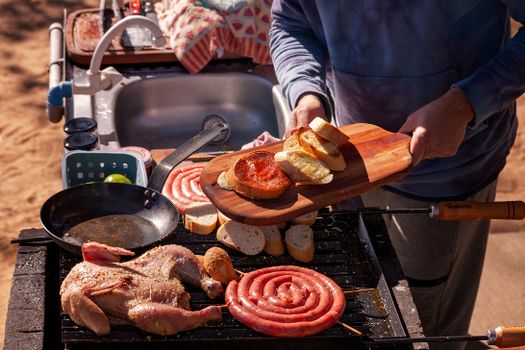 A close-up of a person grilling sausages, chicken, and bread outdoors, creating a delicious summer barbecue.