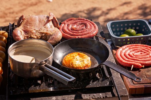 Outdoor barbecue setup with chicken, sausages, and grilling pans.