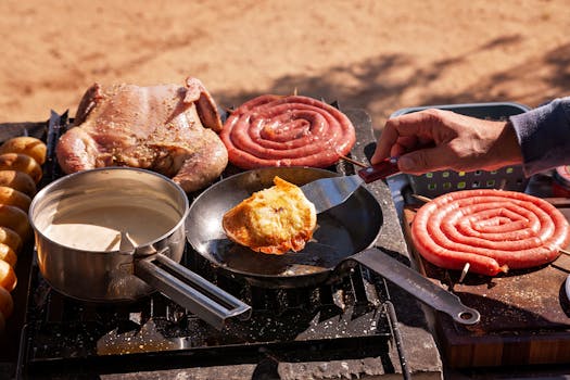 A hand cooking food outdoors with chicken, sausages, and sauce in a rustic setting.