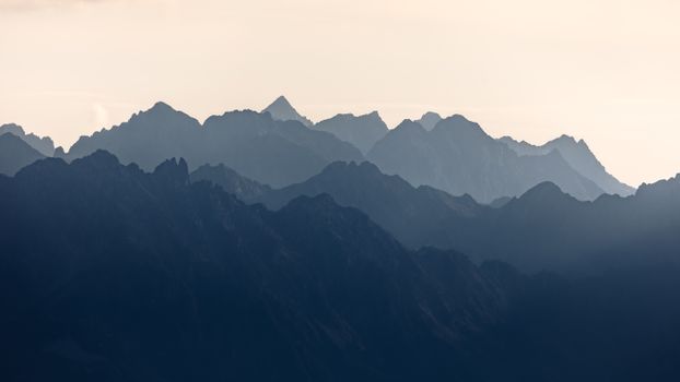 Silhouetted mountain peaks layered against a misty sky at dusk, creating a serene and dramatic landscape.