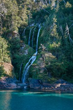 A beautiful waterfall cascading into a clear blue river in Bariloche, Argentina.