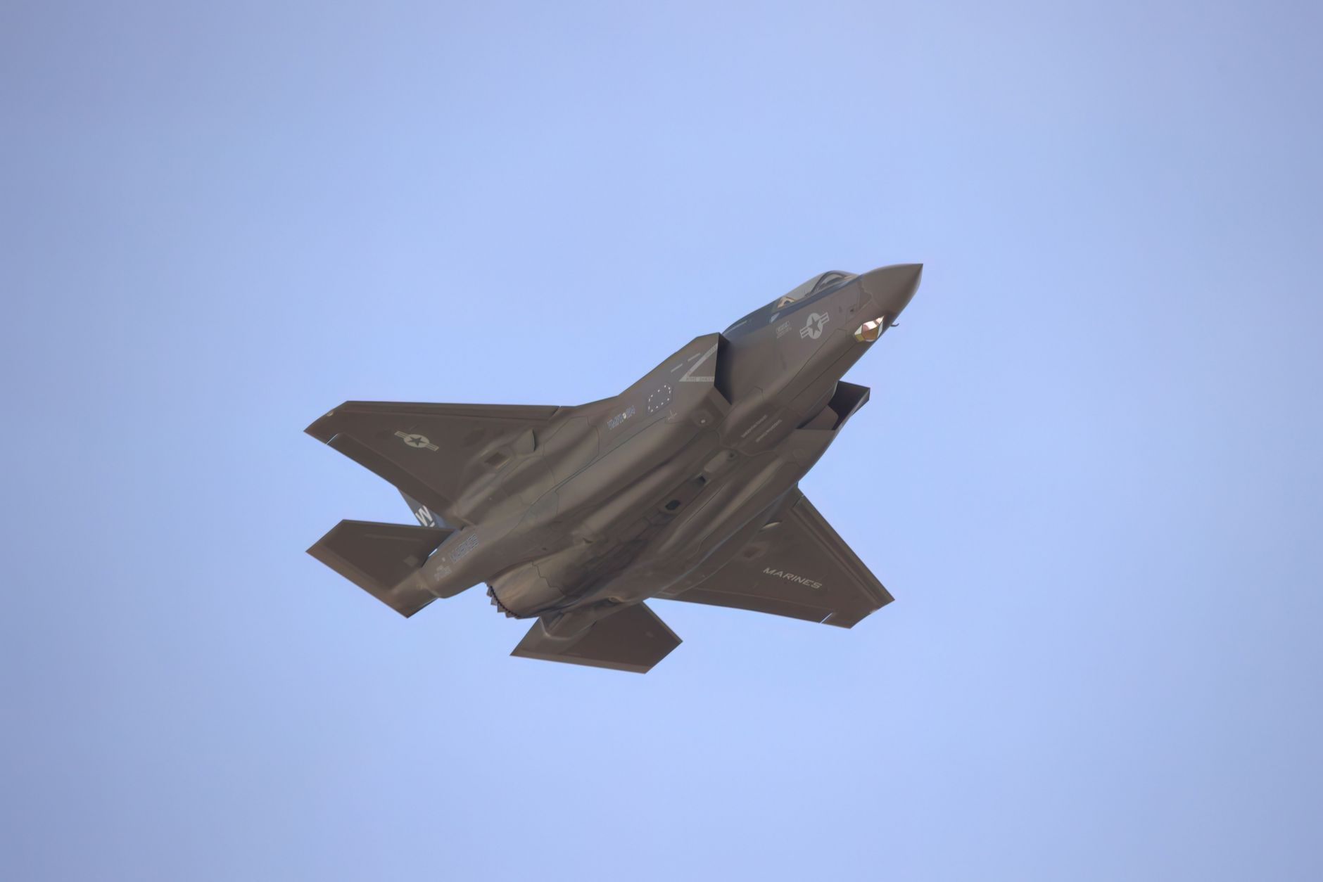 A military jet soaring through a clear blue sky, captured from below, showcasing its sleek design.