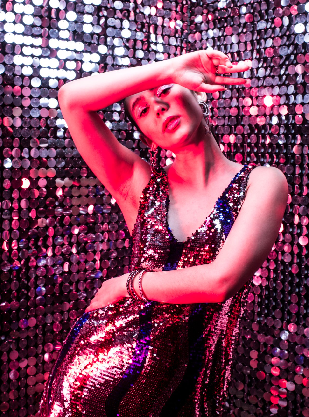 Woman in a silver and pink sequin outfit posing against a sparkling disco wall at a pop concert