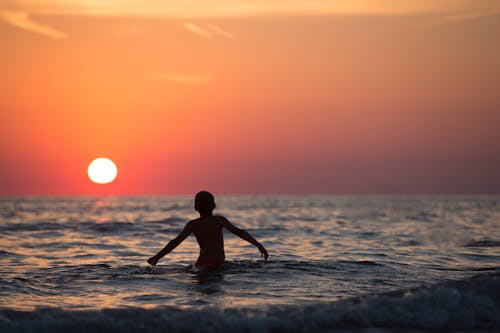 Silhouette Photo of Child on Body of Water during Golden Hour